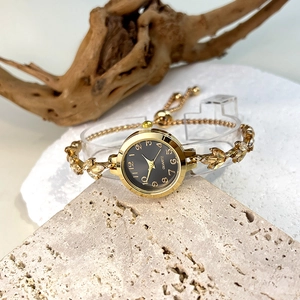 Close-up of golden leaf bracelet watch with rhinestones on a beige stone surface