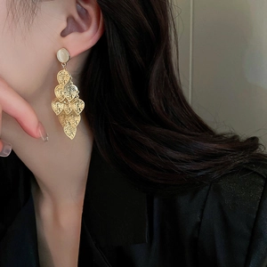 Detail of long gold tassel earrings with hollow leaf design and white opal stones