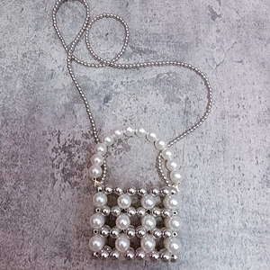 Detail of handmade mini beaded bag with white pearls and silver beads on a stone background
