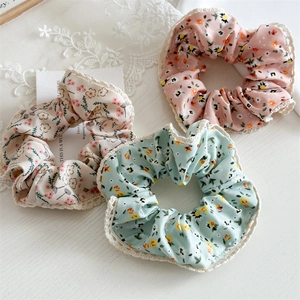 Flat lay of pink, beige, and mint green floral scrunchies with elegant lace trim