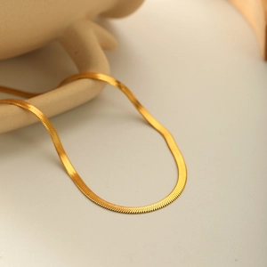 Elegant gold flat snake chain necklace presented against a minimalist ceramic background