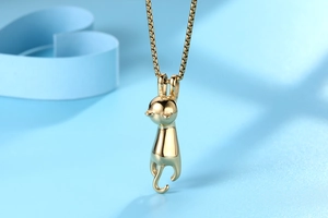 Macro detail of a polished golden cat pendant and delicate box chain on a blue background