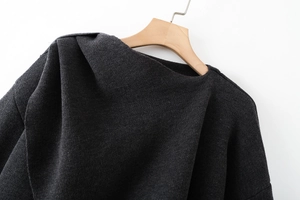 Detail of a dark grey knit poncho featuring an asymmetric neckline and fine knit texture