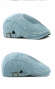 Detail of light blue washed denim flat cap showing textured side weaving and bronze metal buckle