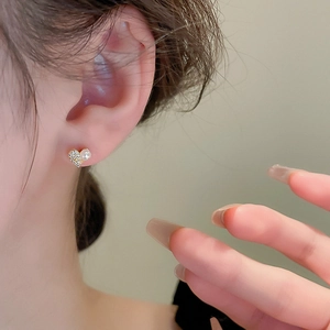 Close-up of heart-shaped gold stud earring with cubic zirconia and a white pearl detail
