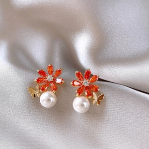 Gros plan de boucles d'oreilles fleurs orange avec perles blanches et papillon doré sur soie