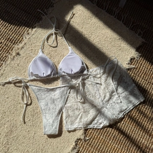 Detailed flat lay of white lace three-piece bikini set with sheer mesh shorts