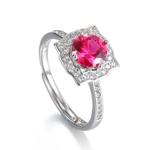 Close-up of a silver ring featuring a round red gemstone surrounded by sparkling diamonds