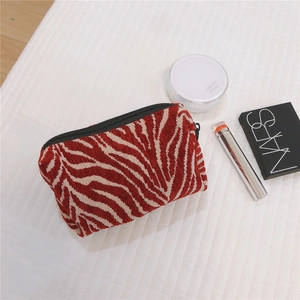 Zebra print cosmetic bag detail with black zipper and makeup accessories on white fabric