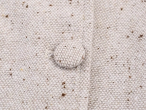 Gros plan sur la texture du tweed crème et le détail du bouton recouvert de tissu