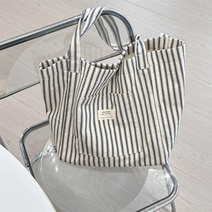 Detail of blue and white striped canvas tote bag on a modern transparent chair