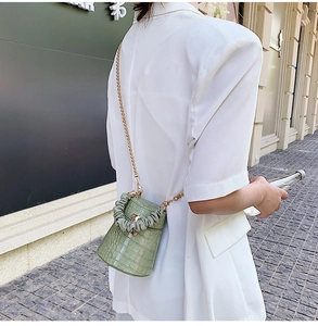 Close-up of green crocodile pattern bucket bag with gold chain strap in city setting