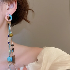 Detail of bohemian drop earrings with turquoise beads, wood accents, and tassels on a model