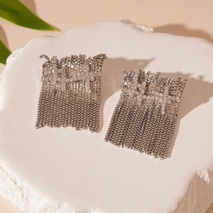 Detailed close-up of sparkling silver fringe earrings with rhinestones on stone background
