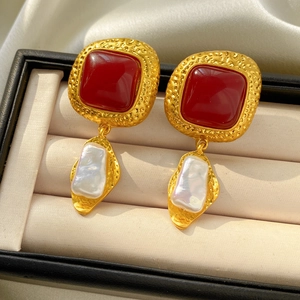 Detailed shot of vintage square red gemstone earrings with baroque pearls on satin fabric