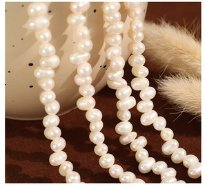Macro shot of white freshwater baroque pearl necklace on ceramic bowl with feathers