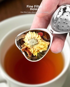Macro shot of heart-shaped stainless steel tea infuser with fine mesh holes and herbs
