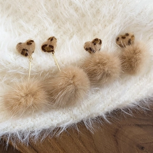 Detail of leopard print heart earrings with khaki pom-poms on white faux fur background