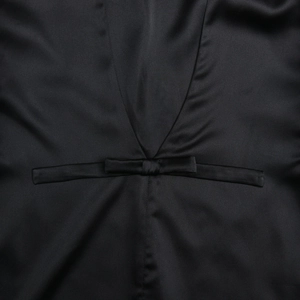 Detalle de elegante minivestido de satén negro con escote en V y pequeño lazo decorativo