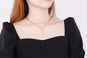 Detail of a double-layered gold feather pendant necklace worn by a fashion model
