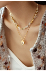 Detail of layered gold necklace with irregular natural stones and white heart pendant