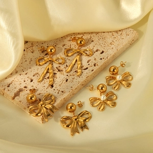 Detail of three gold bow earrings with pearls and tassels on a stone surface