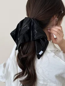 Detail of a large black satin oversized scrunchie with a silk-like glossy finish and tag