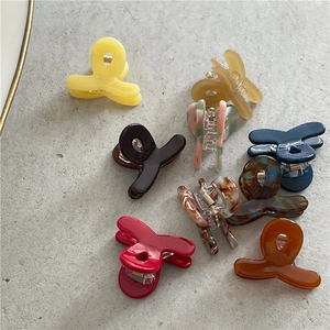 Top view of eight colorful acetate hair claws in various patterns on a grey surface