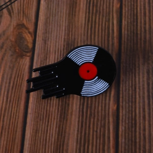 Detailed view of an enamel vinyl record pin with a melting effect on dark wood