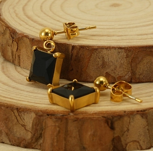 Macro view of gold square black zircon earrings on a rustic wood slice background