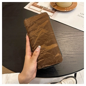 Brown long zipper wallet featuring unique wrinkled paper-texture held in hand at a cafe