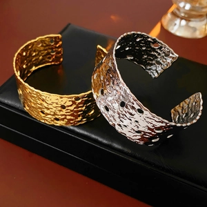 Detail of wide open bangles featuring hammered texture and circular cutouts in gold and silver