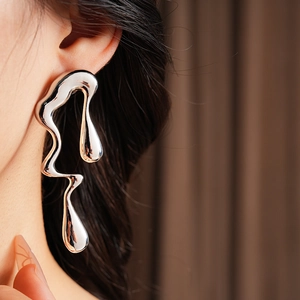 Gros plan d'un mannequin portant des boucles d'oreilles argentées en métal liquide irrégulier