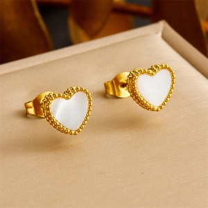 Golden heart earrings with white inlay and beaded edges on a beige jewelry cushion