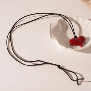Detail view of red heart pendant necklace with bow accent on a white shell tray