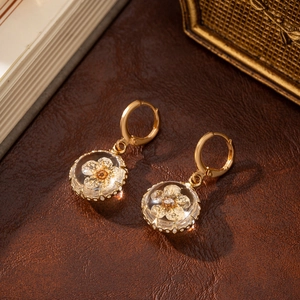 Detail of gold hoop earring featuring clear glass orb with preserved white flower inside