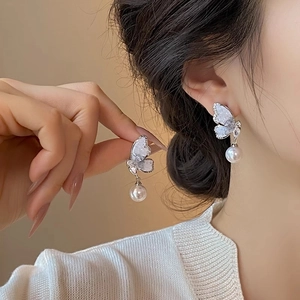 Close-up of elegant butterfly earrings with sparkling zircon and hanging pearl detail