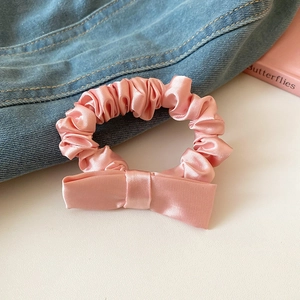 Detailed view of pink satin bow scrunchie showing fabric texture and pleated design