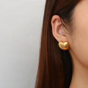 Close-up of golden heart-shaped stud earrings with textured finish on a model's ear