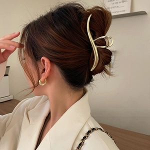 Detail showing a large golden metal hair claw clip and hoop earrings on a model
