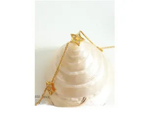 Detailed close-up of 18K gold-plated star pendants with cubic zirconia on a shell