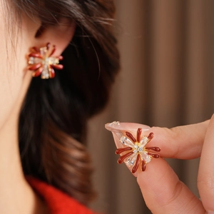 Macro shot of red enamel flower earrings with zircon center inlay on a female model