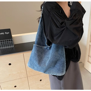 Detail of soft blue denim hobo bag worn as a shoulder tote in a natural indoor setting