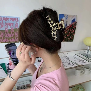 Detail of large gold metallic shark hair clip with hollow star design on female model