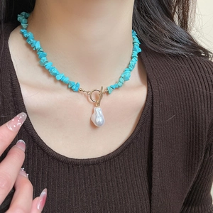 Close-up of turquoise beaded necklace with baroque pearl pendant and gold toggle clasp