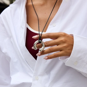 Detail of a silver horseshoe pendant with black cord necklace worn by a fashion model