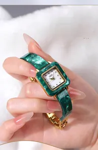 Detail eines luxuriösen smaragdgrünen Harz- und Goldmetallarmbands an einer quadratischen Uhr