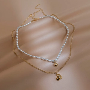 Detail of layered gold heart pendant and pearl necklace on champagne silk background