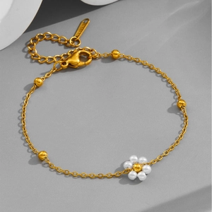 Elegant gold-tone stainless steel daisy bracelet with white pearls on a grey stone base