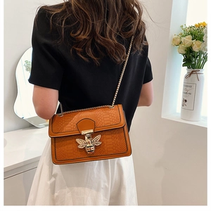 Detail of orange-brown snake skin texture bag with a gold bee buckle and chain strap